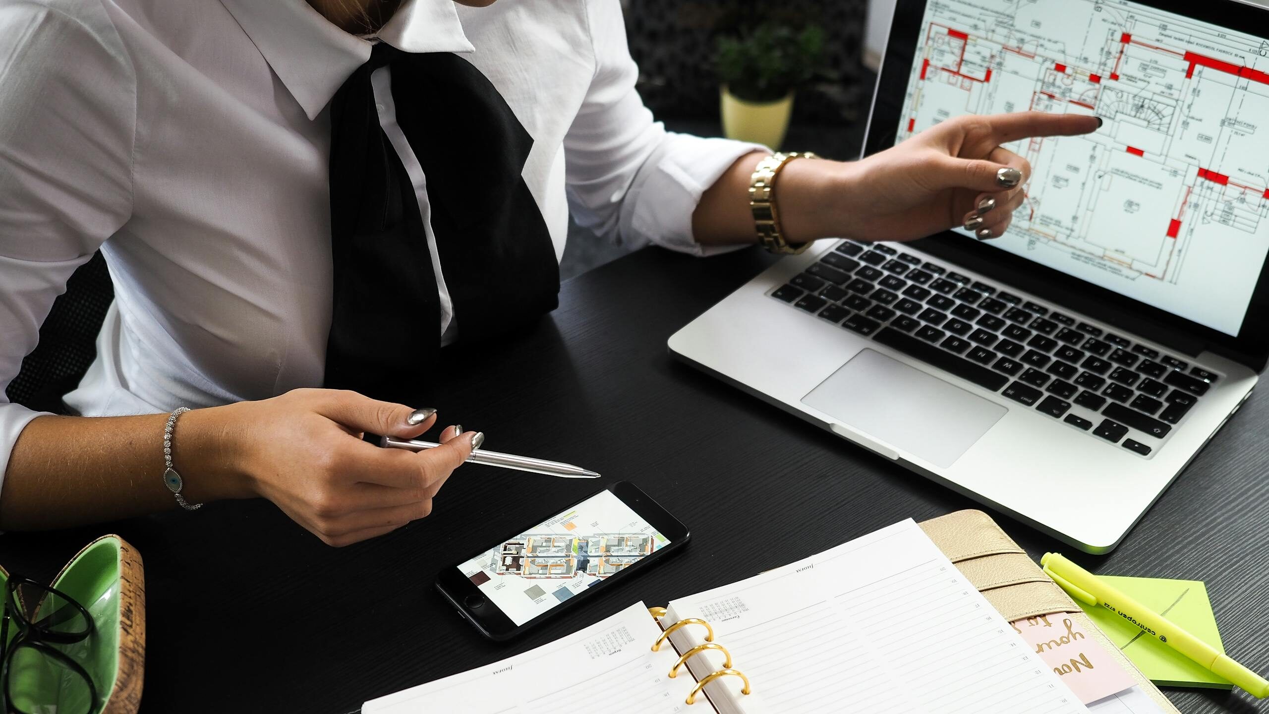 A business professional working on real estate project plans using multiple devices in an office setting.